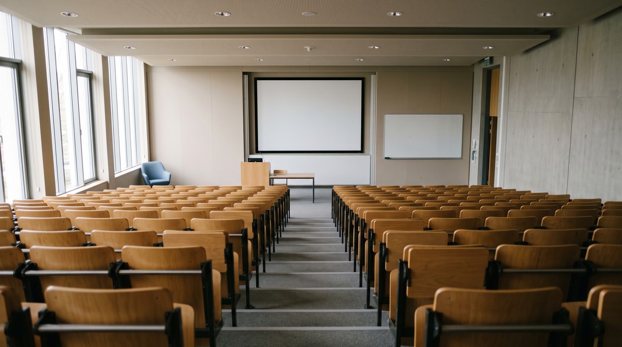 Empty lecture theatre with a blank projection screen and whiteboard at the front